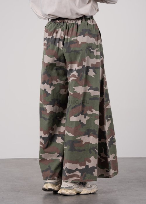 Szerokie spodnie damskie w militarny wzór moro z wysokim stanem i zakładkami w pasie, w stylizacji z paskiem i sneakersami.