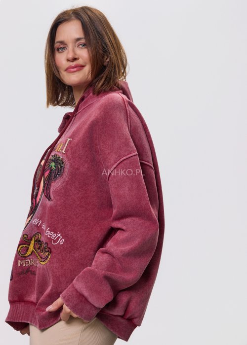 Bordowa bluza z kapturem o luźnym kroju, z dużą artystyczną grafiką postaci i dekoracyjnymi napisami na przodzie; modelka trzyma kaptur, całość sfotografowana na jasnym, neutralnym tle