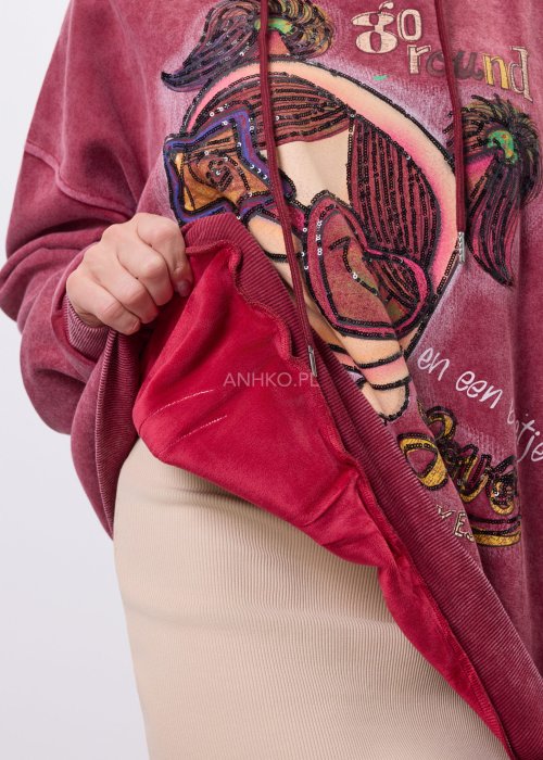 Bordowa bluza z kapturem o luźnym kroju, z dużą artystyczną grafiką postaci i dekoracyjnymi napisami na przodzie; modelka trzyma kaptur, całość sfotografowana na jasnym, neutralnym tle