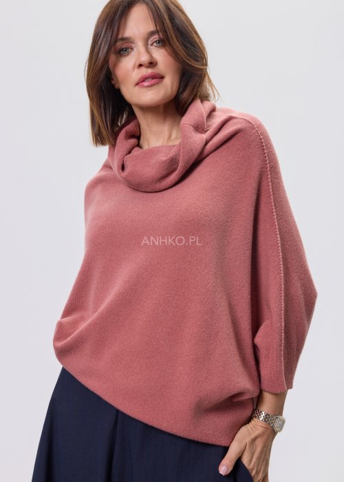 Sweter oversize w kolorze brudnego różu z szerokim kołnierzem typu komin i luźnym krojem poncza. Model prezentowany w stylizacji z ciemnym dołem, podkreślający miękką dzianinę i asymetryczny fason.