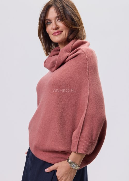 Sweter oversize w kolorze brudnego różu z szerokim kołnierzem typu komin i luźnym krojem poncza. Model prezentowany w stylizacji z ciemnym dołem, podkreślający miękką dzianinę i asymetryczny fason.