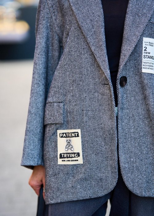 Szara marynarka damska w drobną jodełkę o kroju oversize z ozdobnymi naszywkami, stylizacja z czarnym topem i szerokimi spodniami.