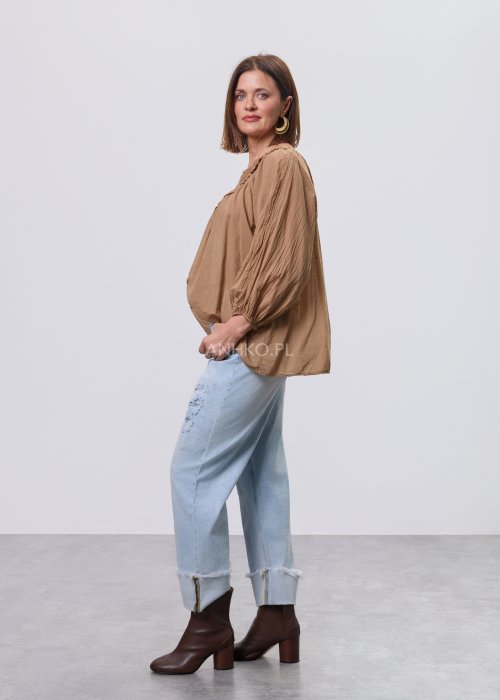 Camelowa bluzka damska z haftem przy dekolcie V i luźnym krojem, zestawiona z jasnymi jeansami w stylizacji casual.