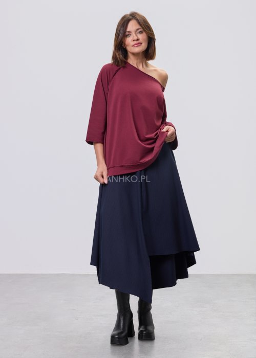 Bordowa bluza damska oversize z raglanowymi rękawami i asymetrycznym dekoltem, stylizowana z granatową spódnicą midi i czarnymi botkami.