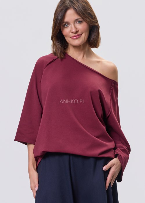 Bordowa bluza damska oversize z raglanowymi rękawami i asymetrycznym dekoltem, stylizowana z granatową spódnicą midi i czarnymi botkami.