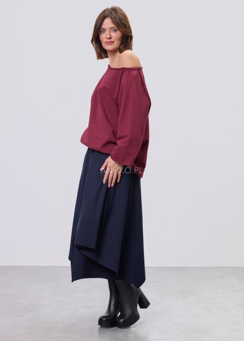 Bordowa bluza damska oversize z raglanowymi rękawami i asymetrycznym dekoltem, stylizowana z granatową spódnicą midi i czarnymi botkami.