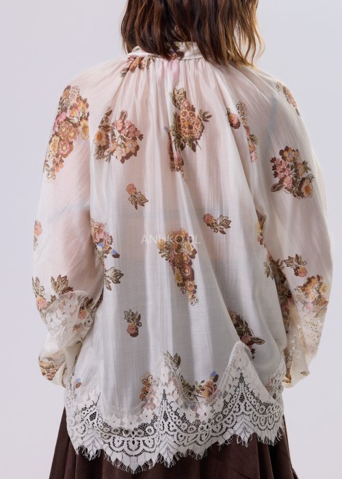 Jasnobeżowa bluzka Liora Bloom z kwiatowym nadrukiem, dekolt V-neck, luźny fason za biodra i koronkowe wykończenie w stylu boho.
