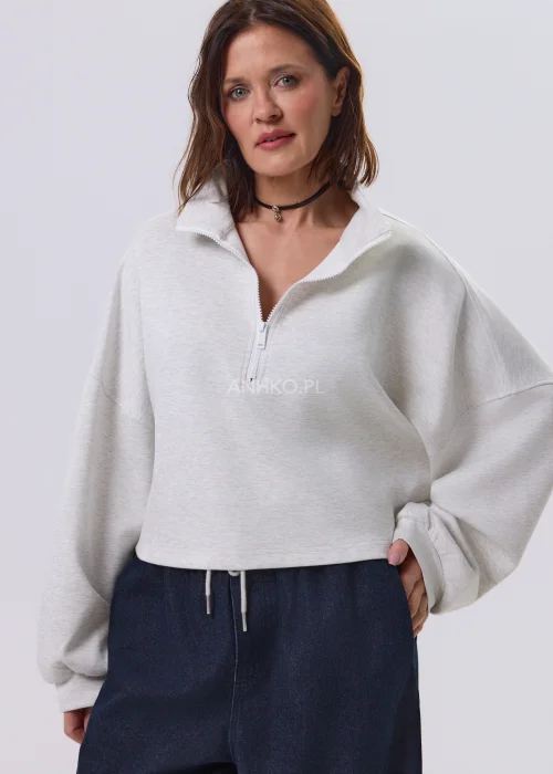 Jasnoszara damska bluza oversize z krótkim fasonem i stójką zapinaną na suwak, zestawiona z ciemnymi spodniami o szerokiej nogawce.