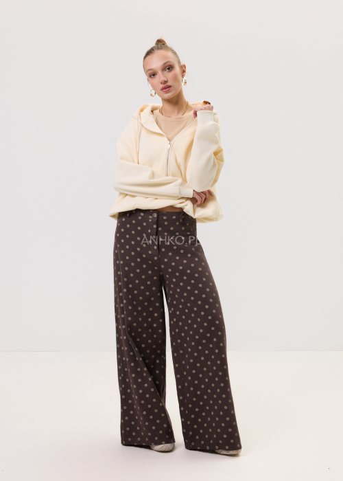 Kremowa damska bluza Creamy Layer o luźnym kroju, z kapturem i krótkim zamkiem przy dekolcie. Model z obniżoną linią ramion i ściągaczami przy rękawach, w stylizacji z brązowymi damskimi spodniami w grochy.