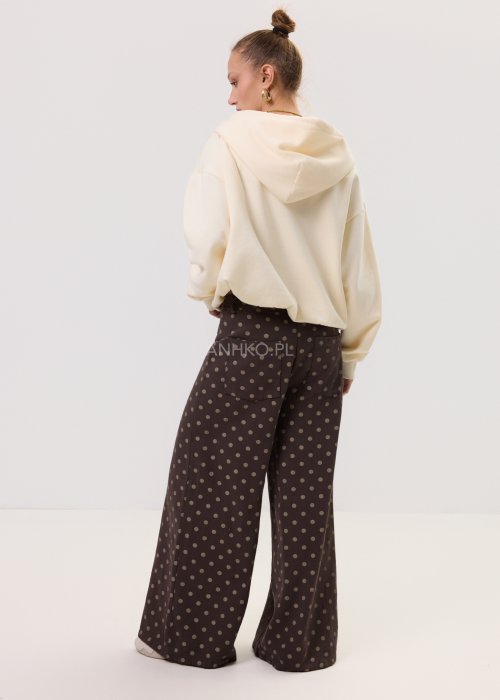 Kremowa damska bluza Creamy Layer o luźnym kroju, z kapturem i krótkim zamkiem przy dekolcie. Model z obniżoną linią ramion i ściągaczami przy rękawach, w stylizacji z brązowymi damskimi spodniami w grochy.