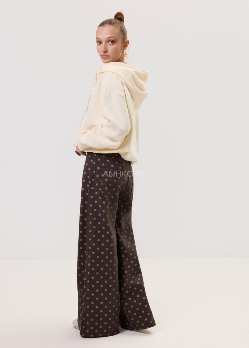 Kremowa damska bluza Creamy Layer o luźnym kroju, z kapturem i krótkim zamkiem przy dekolcie. Model z obniżoną linią ramion i ściągaczami przy rękawach, w stylizacji z brązowymi damskimi spodniami w grochy.