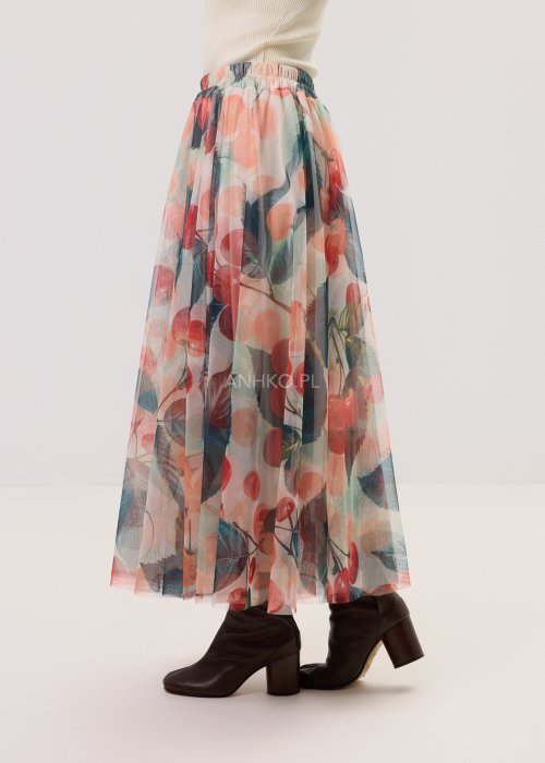 Zwiewna spódnica midi Lunareth Cherry z transparentnej tkaniny w print z wiśniami i liśćmi, z elastyczną gumką w pasie. Stylizacja z pomarańczowym swetrem i brązowymi botkami na obcasie.