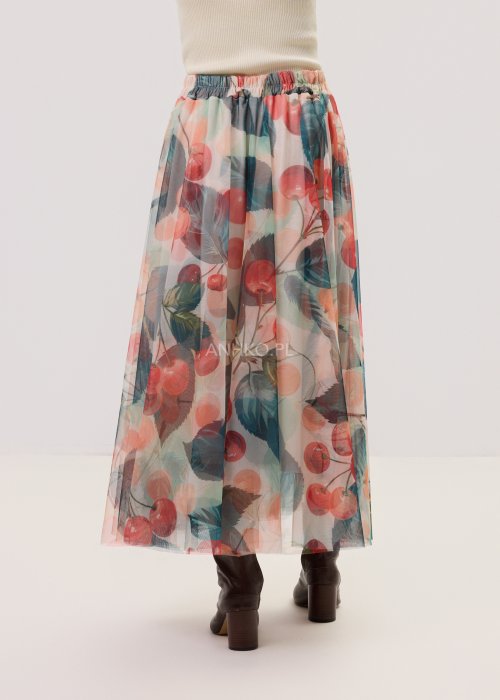 Zwiewna spódnica midi Lunareth Cherry z transparentnej tkaniny w print z wiśniami i liśćmi, z elastyczną gumką w pasie. Stylizacja z pomarańczowym swetrem i brązowymi botkami na obcasie.