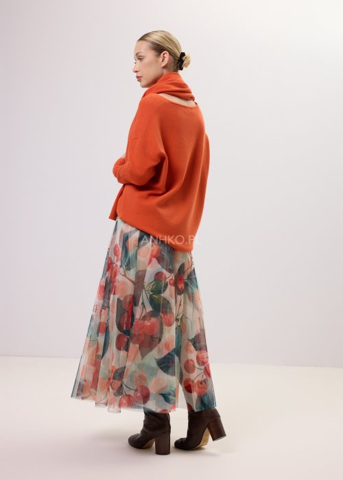 Zwiewna spódnica midi Lunareth Cherry z transparentnej tkaniny w print z wiśniami i liśćmi, z elastyczną gumką w pasie. Stylizacja z pomarańczowym swetrem i brązowymi botkami na obcasie.