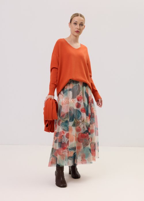 Zwiewna spódnica midi Lunareth Cherry z transparentnej tkaniny w print z wiśniami i liśćmi, z elastyczną gumką w pasie. Stylizacja z pomarańczowym swetrem i brązowymi botkami na obcasie.