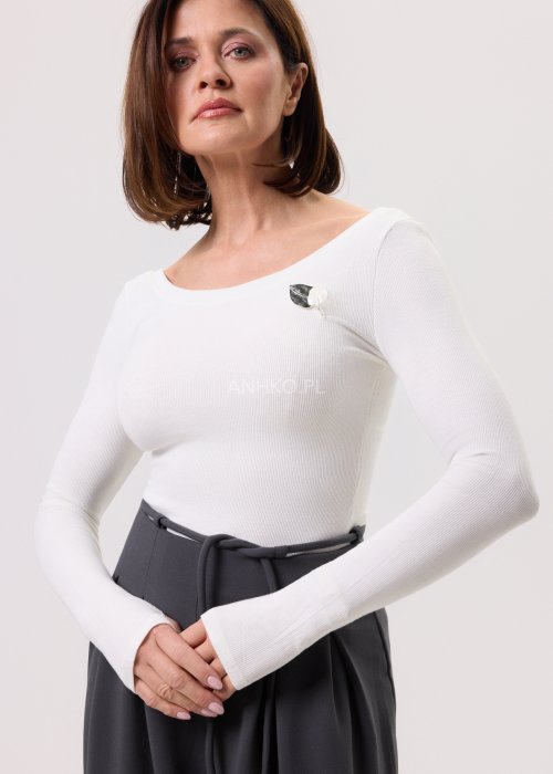 Damska biała bluzka prążkowana z długimi rękawami i subtelną broszką, zestawiona z elegancką spódnicą.
