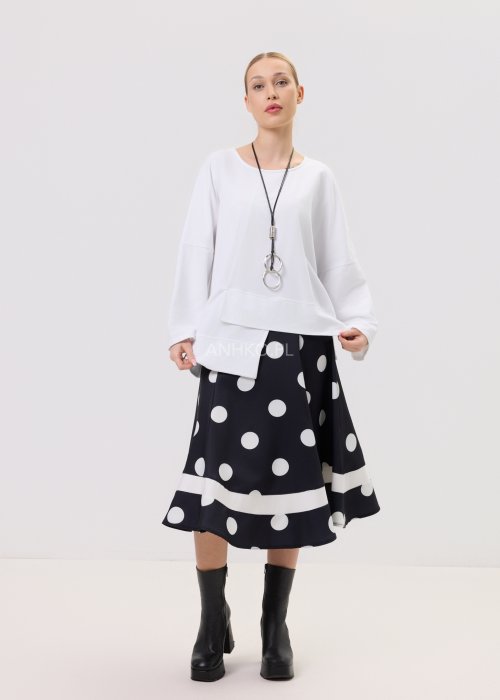 Biała bluza oversize damska z asymetrycznym dołem i szerokim rękawem. Stylizacja z czarną spódnicą w grochy w nowoczesnym, minimalistycznym stylu.