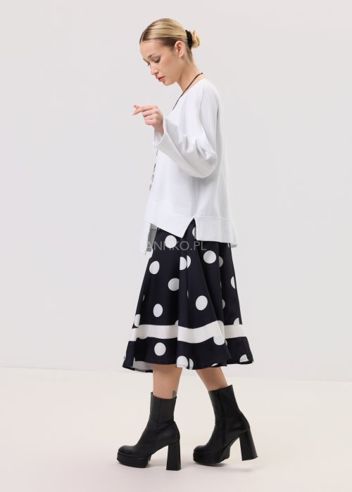 Biała bluza oversize damska z asymetrycznym dołem i szerokim rękawem. Stylizacja z czarną spódnicą w grochy w nowoczesnym, minimalistycznym stylu.