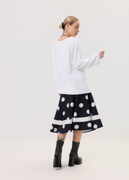 Biała bluza oversize damska z asymetrycznym dołem i szerokim rękawem. Stylizacja z czarną spódnicą w grochy w nowoczesnym, minimalistycznym stylu.