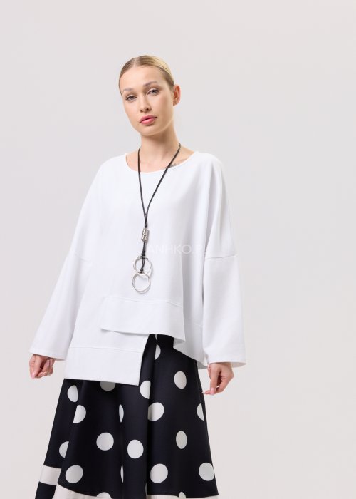Biała bluza oversize damska z asymetrycznym dołem i szerokim rękawem. Stylizacja z czarną spódnicą w grochy w nowoczesnym, minimalistycznym stylu.