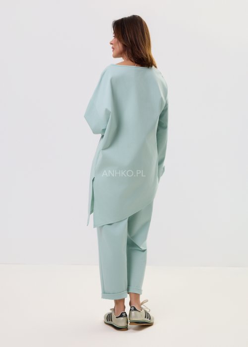 Damskie miętowe spodnie Starola Rose z podwiniętą nogawką i eleganckim paskiem, luźniejszy fason z zakładkami z przodu, w casualowej stylizacji ze sneakersami.