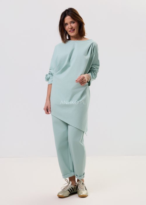 Damskie miętowe spodnie Starola Rose z podwiniętą nogawką i eleganckim paskiem, luźniejszy fason z zakładkami z przodu, w casualowej stylizacji ze sneakersami.