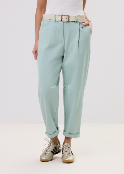 Damskie miętowe spodnie Starola Rose z podwiniętą nogawką i eleganckim paskiem, luźniejszy fason z zakładkami z przodu, w casualowej stylizacji ze sneakersami.