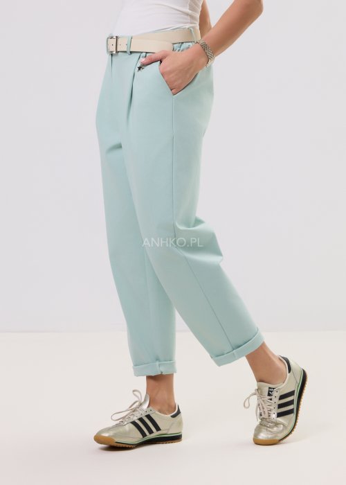 Damskie miętowe spodnie Starola Rose z podwiniętą nogawką i eleganckim paskiem, luźniejszy fason z zakładkami z przodu, w casualowej stylizacji ze sneakersami.