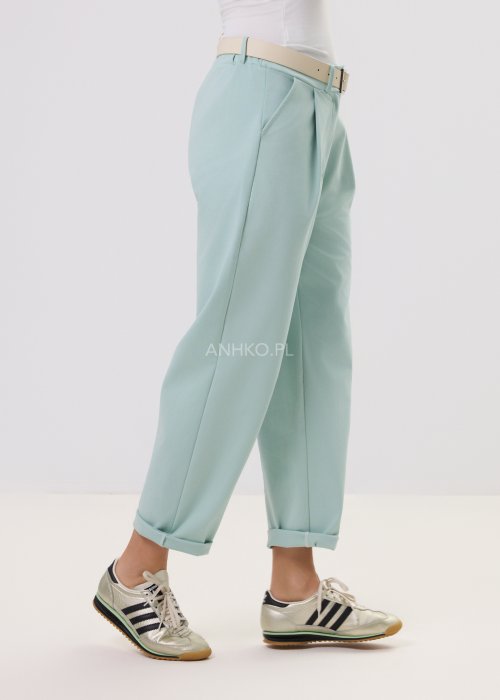 Damskie miętowe spodnie Starola Rose z podwiniętą nogawką i eleganckim paskiem, luźniejszy fason z zakładkami z przodu, w casualowej stylizacji ze sneakersami.