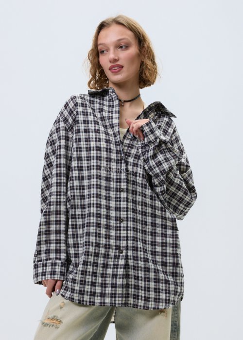 Koszula damska oversize w kratę, zapinana na guziki, stylizowana z jasnymi jeansami z przetarciami.