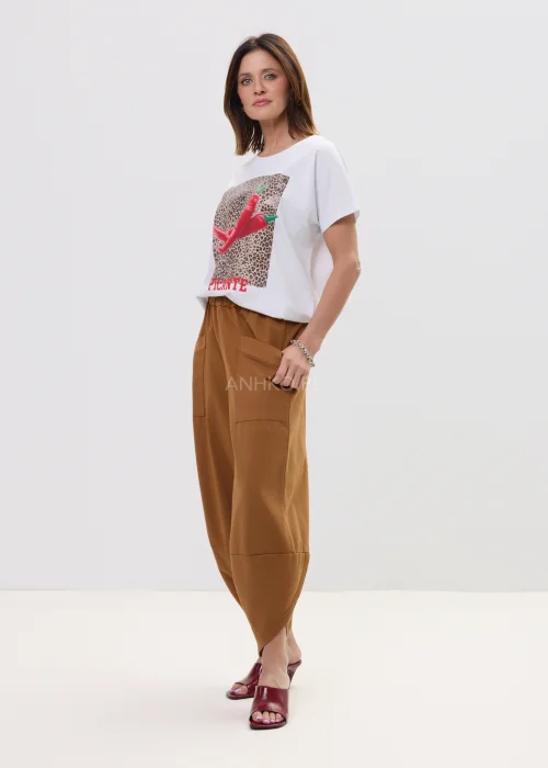 Biały t-shirt z nadrukiem czerwonych papryczek na tle panterki i napisem „PICANTE”, luźny fason – stylizacja z brązowymi spodniami.