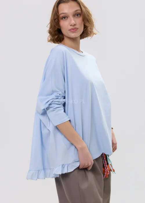 Bluzka damska oversize w jasnoniebieskim kolorze, z dłuższym tyłem i subtelną falbaną przy rękawach, lekka i komfortowa baza do codziennych stylizacji.