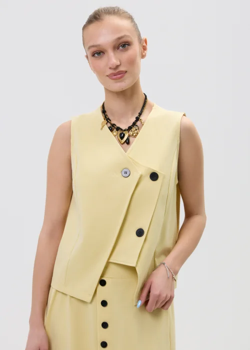 Żółta kamizelka damska o kopertowym kroju z ozdobnymi czarnymi guzikami, elegancka i nowoczesna, w stylizacji z dopasowaną spódnicą.