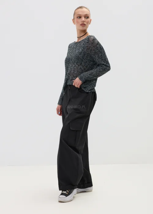 Melanżowy sweter o luźnym kroju z ażurową strukturą, w odcieniach szarości stylizowany z czarnymi spodniami w minimalistycznym looku.