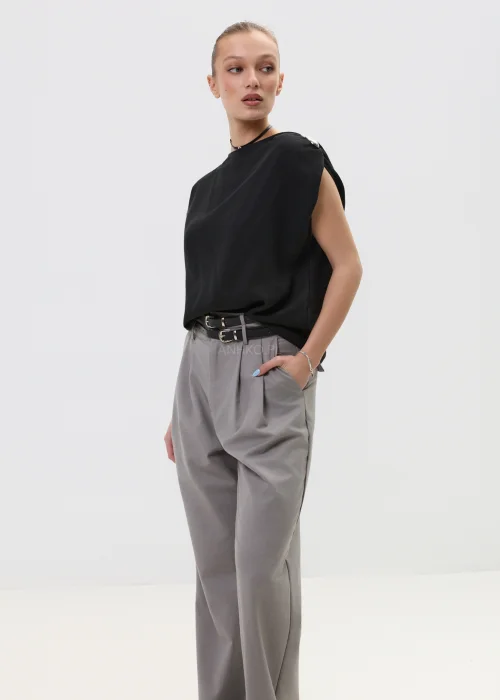Czarna bluzka damska bez rękawów z luźnym krojem i ozdobnym zapięciem na ramieniu, elegancka minimalistyczna stylizacja.