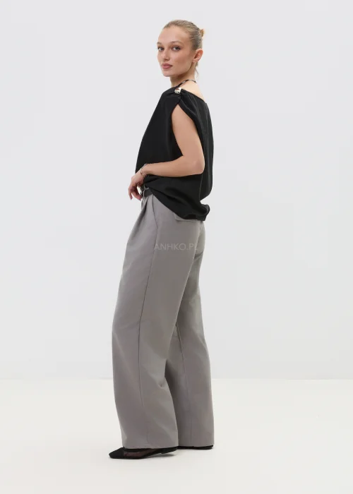 Czarna bluzka damska bez rękawów z luźnym krojem i ozdobnym zapięciem na ramieniu, elegancka minimalistyczna stylizacja.