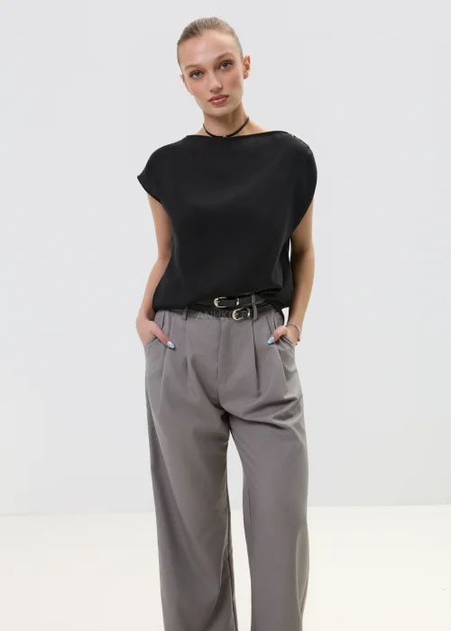 Czarna bluzka damska bez rękawów z luźnym krojem i ozdobnym zapięciem na ramieniu, elegancka minimalistyczna stylizacja.