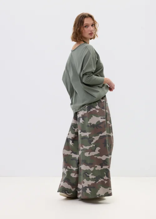 Szerokie spodnie damskie w militarny wzór moro z wysokim stanem i zakładkami w pasie, w stylizacji z paskiem i sneakersami.