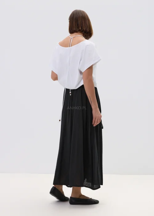 Biała bluzka o luźnym kroju z krótkim rękawem, z ozdobnym dekoltem wykończonym koralikami, stylizowana z czarną spódnicą w minimalistycznym, eleganckim wydaniu.