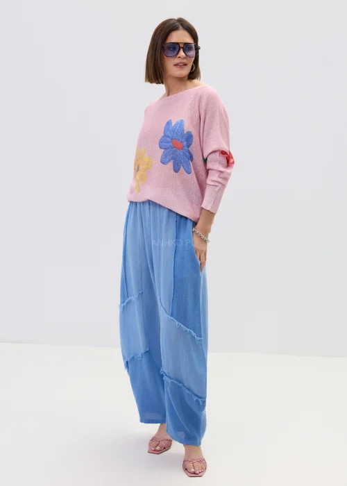 Pudrowo różowy sweter o lekkim, luźnym splocie z kolorowym motywem kwiatów, zestawiony z niebieską spódnicą w casualowej stylizacji.