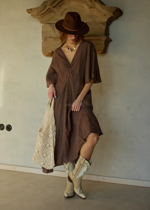 Beżowa torba ażurowa z plecionym wzorem geometrycznym, duża i miękka, noszona na ramieniu w stylizacji boho z sukienką i kapeluszem.