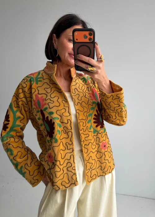 Jasnobrązowy żakiet boho z kolorowymi haftami kwiatowymi i dekoracyjną stójką. Krótki model o artystycznym charakterze inspirowanym folklorem.