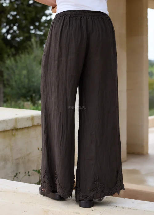 Ciemnobrązowe lniane spodnie palazzo z ozdobną koronką przy nogawkach. Szeroki, swobodny fason z elastycznym pasem zapewnia komfort noszenia i eleganckie wykończenie w stylu boho.