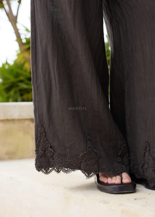 Ciemnobrązowe lniane spodnie palazzo z ozdobną koronką przy nogawkach. Szeroki, swobodny fason z elastycznym pasem zapewnia komfort noszenia i eleganckie wykończenie w stylu boho.