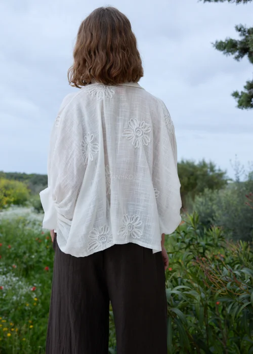 Biała koszula boho z haftowanymi kwiatami i ozdobnymi zapięciami w kształcie rozgwiazd. Zwiewny fason wiązany w talii, zestawiony z ciemną spódnicą maxi.