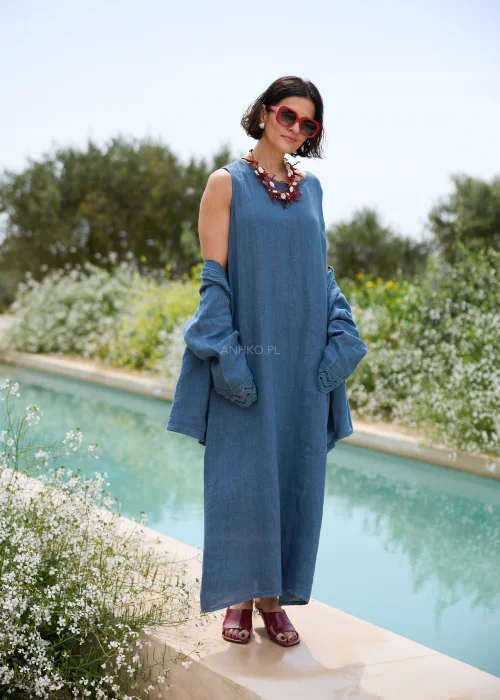 Niebieska lniana sukienka maxi z lekkim kardiganem wykończonym koronkowymi detalami. Elegancka, swobodna stylizacja w denimowym odcieniu, uzupełniona wyrazistą biżuterią i czerwonymi dodatkami.