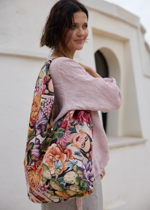 Torebka shopper z kolorowym gobelinowym wzorem przedstawiającym kwiaty, liście i artystyczne motywy na jasnym tle. Duża materiałowa torba z krótką rączką doskonale uzupełnia stylizacje boho, casual i art fashion.