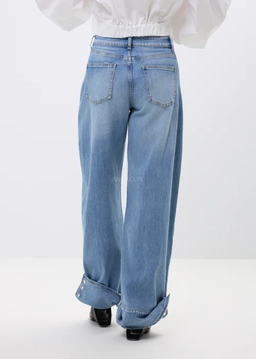 Spodnie jeansowe wide leg w jasnoniebieskim odcieniu z efektownymi mankietami zapinanymi na napy. Szerokie nogawki i nowoczesne detale nadają modelowi modny, swobodny charakter.