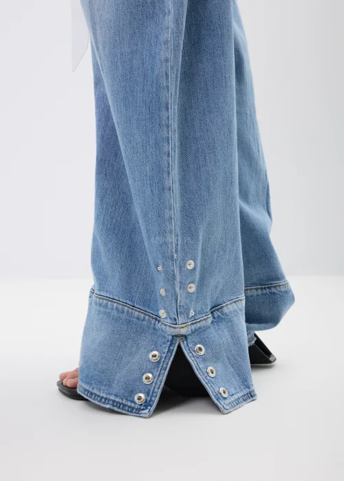 Spodnie jeansowe wide leg w jasnoniebieskim odcieniu z efektownymi mankietami zapinanymi na napy. Szerokie nogawki i nowoczesne detale nadają modelowi modny, swobodny charakter.
