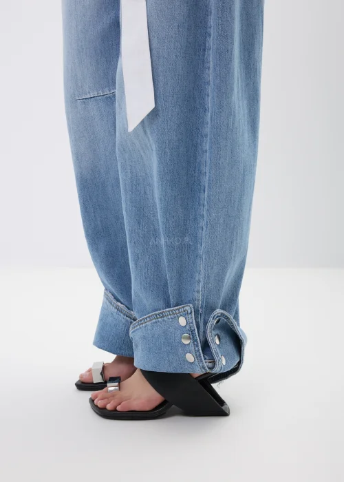 Spodnie jeansowe wide leg w jasnoniebieskim odcieniu z efektownymi mankietami zapinanymi na napy. Szerokie nogawki i nowoczesne detale nadają modelowi modny, swobodny charakter.